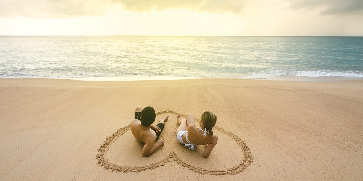 pereja-joven-de-novios-en-la-playa-formando-con-sus-manos-un-corazon
